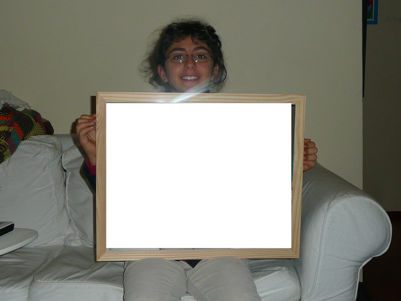 A photograph of a person sitting on a couch, holding up an empty rectangular picture frame.
